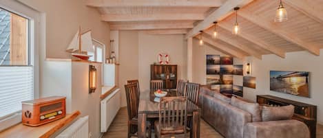 A cozy interior with a wooden ceiling, a dining table with chairs, a sofa, and a bookshelf.