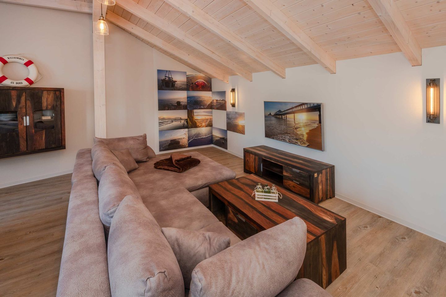 Een moderne woonkamer met een grote hoekbank, een houten salontafel en een wandtelevisie.