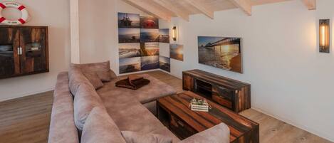 Een moderne woonkamer met een grote hoekbank, een houten salontafel en een wandtelevisie.