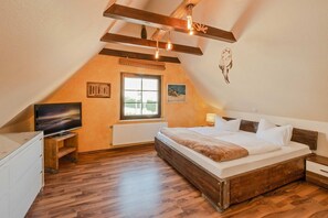 Un dormitorio con una cama, televisión, ventana y vigas de madera en el techo.