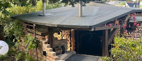 A small, rustic outdoor structure with a brick wall, a wooden door, and a metal roof.