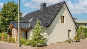 Ein eingeschossiges Haus mit geneigtem Dach, einem Schornstein und einer kleinen Veranda mit Holzgeländer.