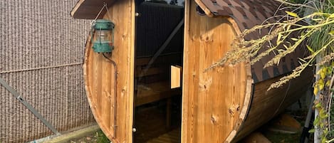 Une structure en forme de tonneau, faite de bois, avec une porte, une lanterne suspendue et une petite fenêtre.
