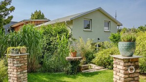 Ein Haus mit grüner Fassade, einer Ziegelgartenmauer und Blumentöpfen darauf.