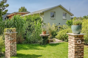 Ein Haus mit grüner Fassade, einer Ziegelgartenmauer und Blumentöpfen darauf.