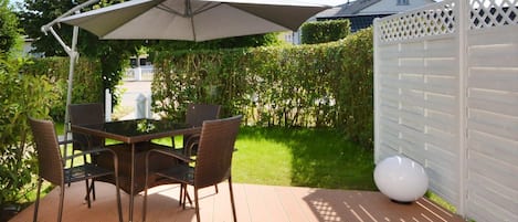 An outdoor patio with a table and chairs, a large umbrella, and a white fence.