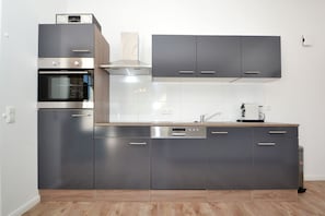 A modern kitchen with stainless steel appliances, grey cabinetry, and a wooden countertop.