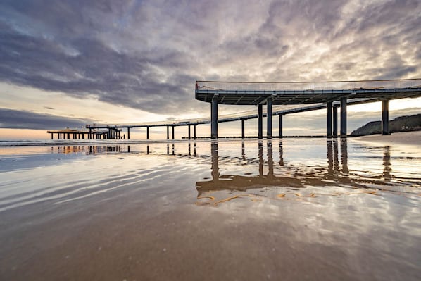 A pier extending into calm waters with a cloudy sky above.