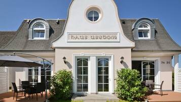 A two-story building with a central entrance, a covered patio area with outdoor seating, and a sign above the entrance.