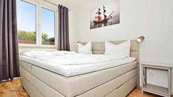A bedroom with a large bed, a bedside table, a nightstand, and a window with curtains.