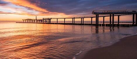 A pier extending into calm waters with a sunset in the background.