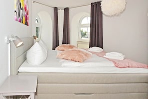 A bedroom with a bed, a bedside table, a lamp, and a window with curtains. - Comfortable vacation apartment in Koserow with a terrace—just 350 m from the beach—House (Koserow)