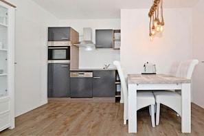A compact kitchen with modern appliances, a dining table with chairs, and a hanging light fixture.