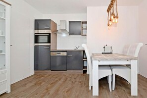 A compact kitchen with modern appliances, a dining table with chairs, and a hanging light fixture. - Comfortable vacation apartment in Koserow with a terrace—just 350 m from the beach—House (Koserow)