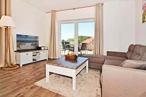 A living room with a television, a sofa, a coffee table, and a view of the outdoors.