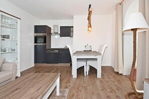 A modern kitchen with dark cabinets, a built-in oven, and a dining area with a wooden table and white chairs.