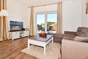 A living room with a television, a sofa, a coffee table, and a view of the outdoors. - Comfortable vacation apartment in Koserow with a terrace—just 350 m from the beach—House (Koserow)