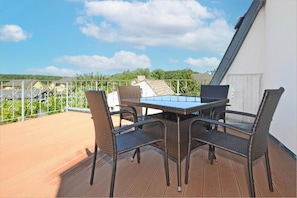 Eine Terrasse mit Tisch und Stühlen, ein Holzboden und eine Aussicht auf Häuser im Hintergrund.