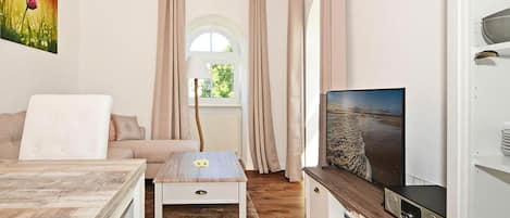 Ein modernes Wohnzimmer mit einer Couch, einem Couchtisch, einem Fernseher und Blick auf einen Strand durch ein Fenster.