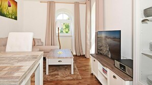 A modern living room with a sofa, coffee table, TV, and a view of a beach through a window.