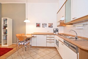 A modern kitchen with white cabinets, a wooden countertop, a built-in dishwasher, and a hanging pendant light.