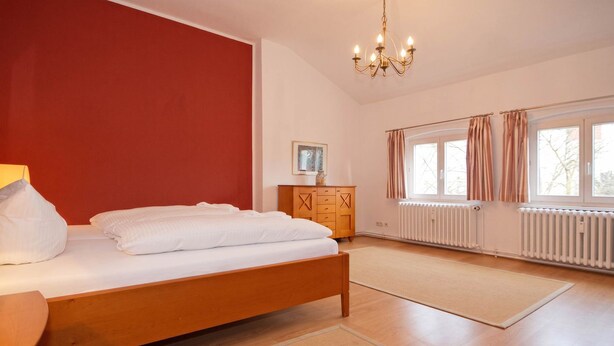 A bedroom with a bed, wooden dresser, and a radiator.