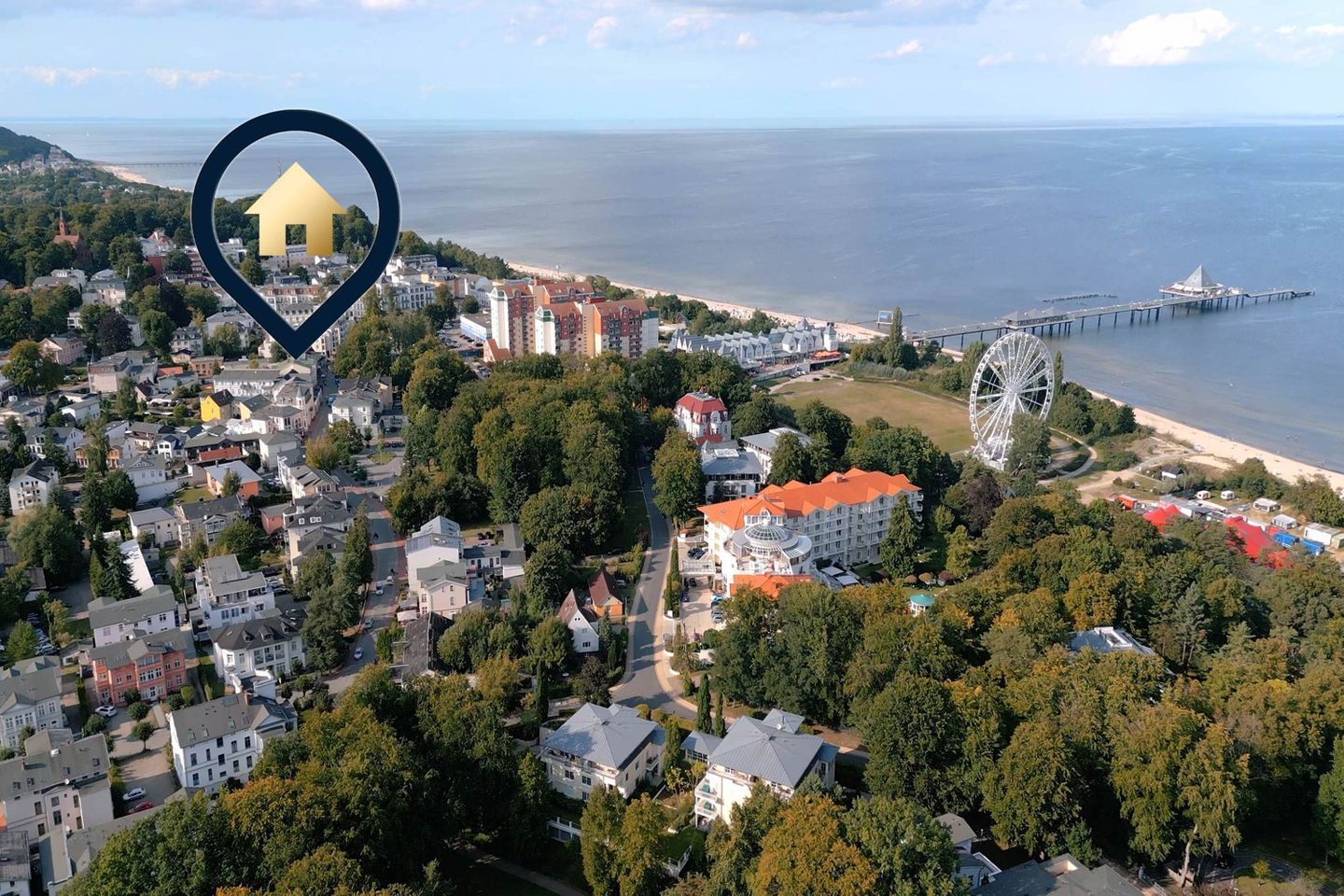 Vista aérea de un pueblo costero con una noria destacada, un muelle y diversos edificios residenciales.