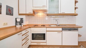 A compact kitchen with white cabinetry, a built-in oven, a dishwasher, and a coffee maker on the countertop.