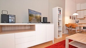 A modern kitchen with white cabinetry, a red rug, and a dining area with wooden chairs.