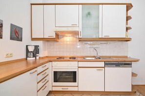 A compact kitchen with white cabinetry, a built-in oven, a dishwasher, and a coffee maker on the countertop.