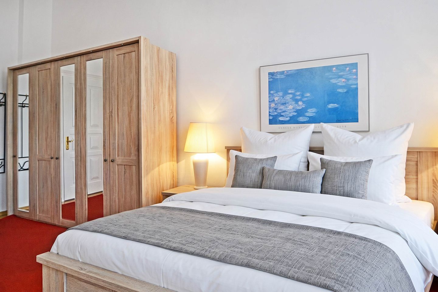 Una habitación de hotel con una cama, una mesita de noche, una lámpara, un armario y un cuadro en la pared.