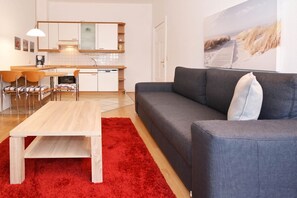 A modern living room with a grey sofa, a wooden coffee table, and a red rug. - Charming vacation apartment in Heringsdorf with balcony, only 200 m from the Baltic Sea beach - (Heringsdorf)