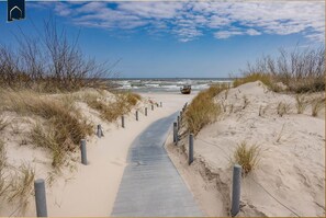 Ein sandiger Strandweg führt zum Meer, im Hintergrund ein Boot.