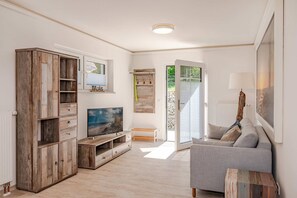 Ein Wohnzimmer mit Fernseher, Holzschrank, grauem Sofa und einem kleinen Tisch.