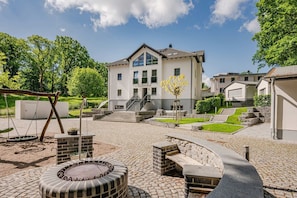 Ein modernes Gebäude mit einer Terrasse, auf der sich eine Schaukel, ein Feuerkorb und eine Treppe zum Eingang befinden.