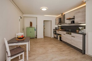 Une cuisine moderne avec un coin repas, dotée d’un parquet en bois de couleur claire, d’un meuble vert et d’un four encastré.
