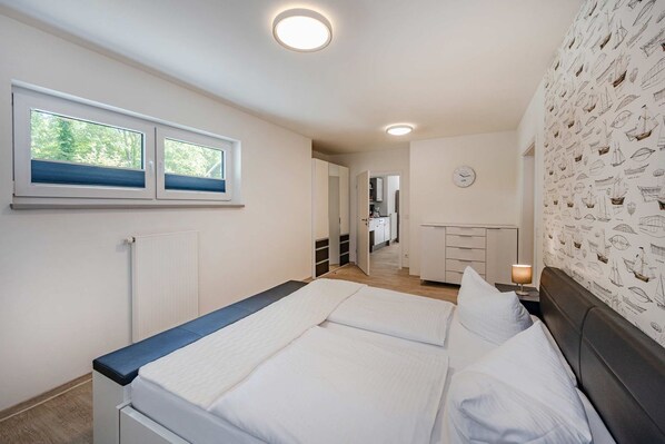 Une chambre avec un lit, une fenêtre, une horloge murale et une vue sur la cuisine.