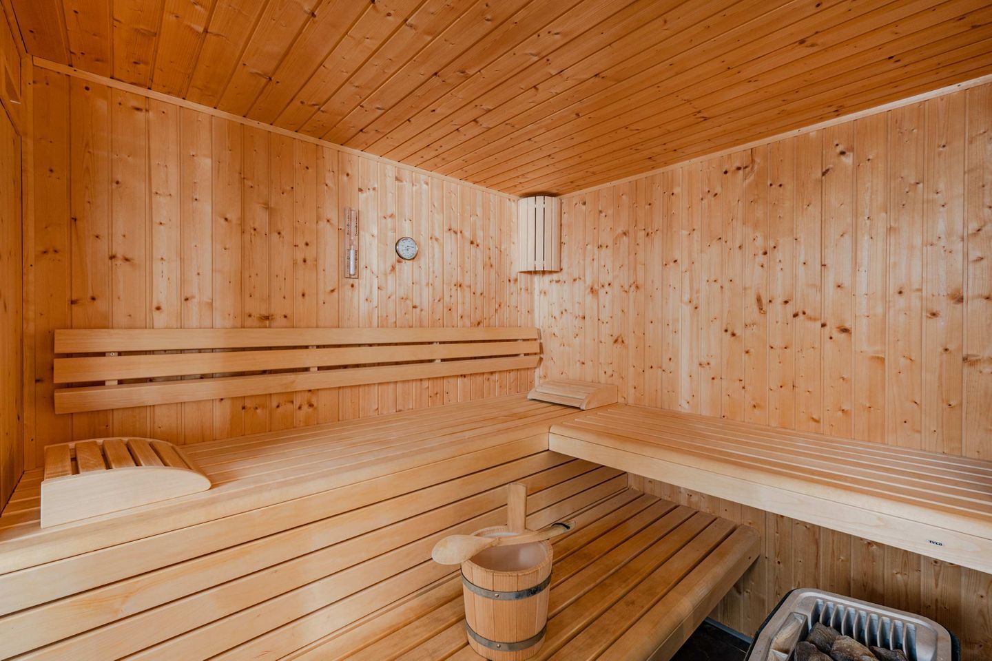 Una sauna de madera con bancos, un cubo y un termómetro en la pared.