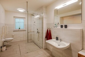 Moderni kylpyhuone, jossa on lasinen suihkuseinä, wc, pesuallas ja ikkuna, josta avautuu näkymä taivaalle.