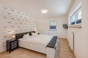 Ein Schlafzimmer mit einem Bett, Nachttischen, einer Wand mit nautisch gestalteter Tapete, einem Fenster und einer Heizung.
