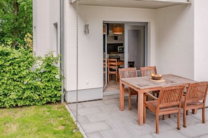 A patio with a wooden table and chairs, a small garden, and a building entrance.