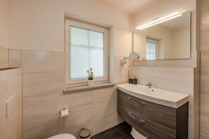 A modern bathroom with a window, a sink, a mirror, and a toilet.