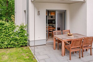A patio with a wooden table and chairs, a small garden, and a building entrance.