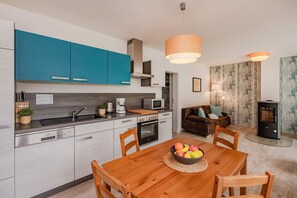 A modern kitchen with teal cabinets, a dining table with chairs, a fruit bowl, and a wood-burning stove. - Modern vacation apartment in Heringsdorf with terrace, only 1000 m from the beach (Heringsdorf)
