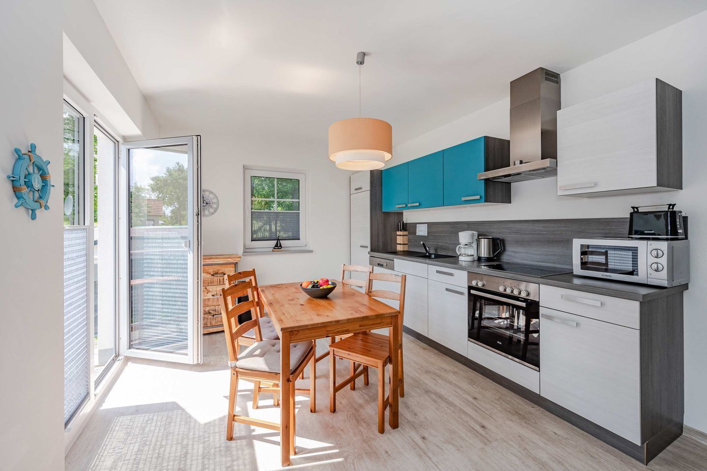 A modern kitchen with a wooden dining table, built-in appliances, and a large window.