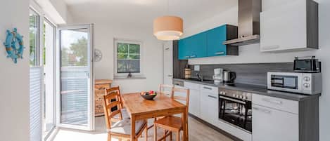 A modern kitchen with a wooden dining table, built-in appliances, and a large window.