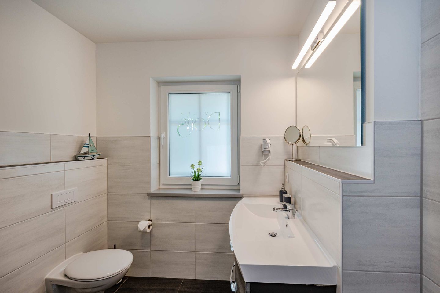 Ein modernes Badezimmer mit Toilette, Waschbecken und Fenster.
