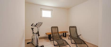 Une pièce dotée d’un ventilateur de plafond, d’un vélo d’exercice, d’une table en bois et de deux fauteuils inclinables.
