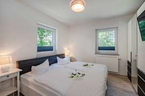 Makuuhuoneessa on kaksi sänkyä, yöpöytä, lamppu, patteri ja ikkuna, josta on näkymä puita kohden.
