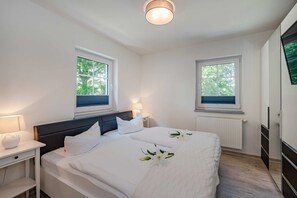 Een slaapkamer met twee bedden, een nachtkastje, een lamp, een radiator en een raam met uitzicht op bomen.